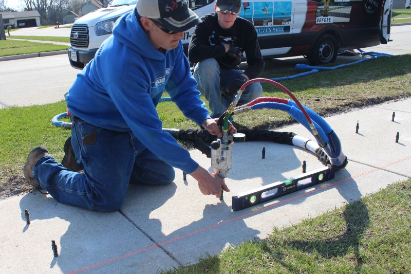 Man injecting polyurethane foam into a concrete slab with an injector gun