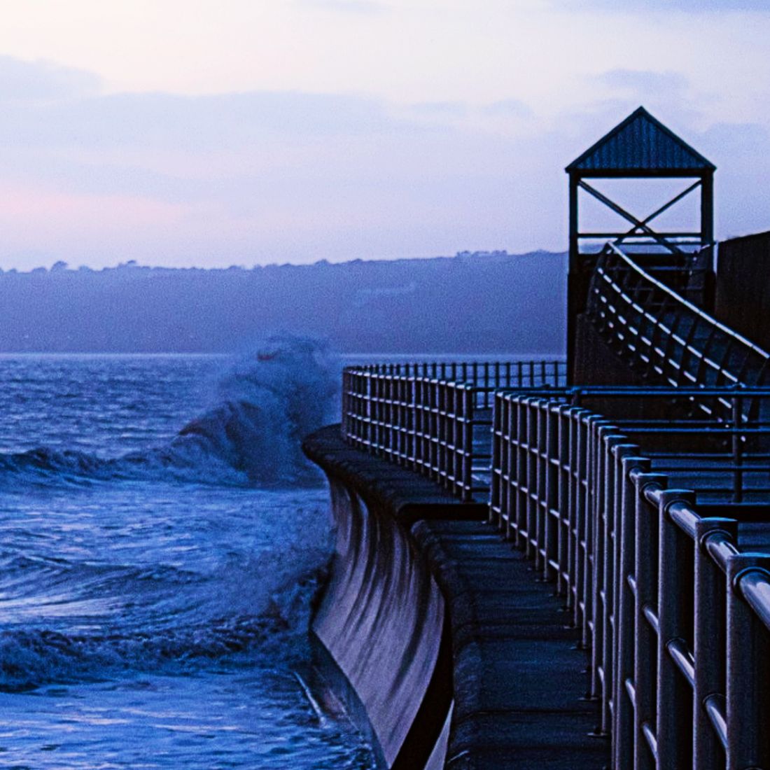 Waves crashing against a seawall with a railing