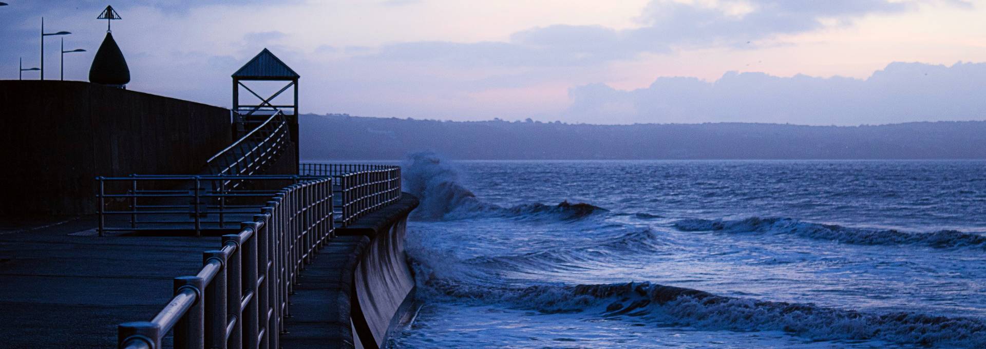 Waves crashing on a seawall with a railing